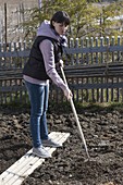 Frau lockert im Frühjahr den Boden als Vorbereitung für Aussaat