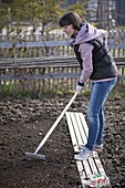 Frau glättet mit einem Rechen im Frühjahr den Boden als Vorbereitung