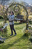 Woman decorating rose arch with eggs, wreath made of Salix (willow)