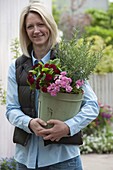 Woman holding pot with rosemary (Rosmarinus) and Primula 'Romance', 'Valentin'.