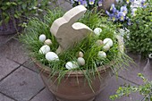 Pot with grass as Easter nest with wooden Easter bunny and Easter eggs