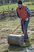 Mann verfestigt und glättet Boden mit einer Gartenwalze