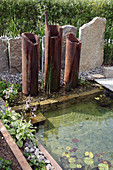 Moderner Teich mit Wasserspiel aus aufgestellten Rohren, Sessel