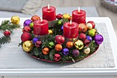 Colourful Advent wreath with red candles in silver holders, colourful baubles