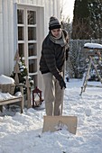 Mann schiebt Schnee mit Schneeschaufel auf der Terrasse