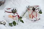 Einmachgläser mit Hedera (Efeu) und roter Schnur als Windlichter im Schnee