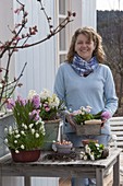Frau arrangiert rosa-weißen Frühlings-Tisch auf der Terrasse