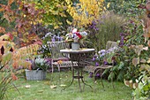 Kleiner Sitzplatz auf Rasen am Herbstbeet mit Astern und Gehoelzen