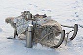 Schlitten mit Lammfell und Thermoskanne im Schnee