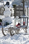 Verschneiter Garten mit Schneemann und Schlitten mit Laternen