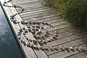 Spirale aus Kieselsteinen gelegt auf Holzsteg am Schwimmteich