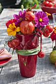 Feurige Tischdeko mit Gemüse und Sommerblumen in roten Bechern