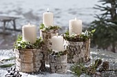weiße Kerzen mit Moos auf Birkenstaemmen