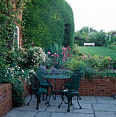 Terrasse mit Tisch und Stühlen neben Beet mit Rosen