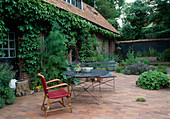 Mit Klinker gepflasterte Terrasse am Haus, Hauswand begrünt mit Parthenocissus (Wildem Wein), Gewürz-Fenchel (Foeniculum) im Beet, Tisch, Bank und Sessel