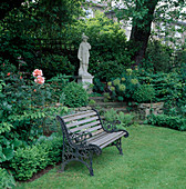 Holzbank und Statue vor Beet mit Rose 'Just Joey' und Euphorbia
