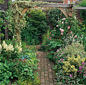 BRICK PATH LEADING TO Water Feature with Pergola ABOVE COVERED IN HEDERA ELEGANTISSIMA. Designer: Roger PLATTS