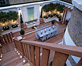 Moderner Dachgarten mit Holzplanken ausgelegt, Glaswasserspiel, Glanzmispeln, silberner Tisch und Stühle