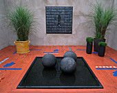 Minimalistisches, quadratisches Wasserbecken mit schwarzen Kugeln und gestrichenem Holzboden, Töpfe mit Miscanthus (Chinaschilf)
