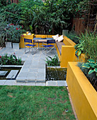 A PLACE TO SIT: Aluminium TABLE AND CHAIRS On Patio SURROUNDED by Yellow RENDERED WALLS with RAISED BEDS AND RILL. Oleander IN GALVANISED CONTAINER. Designer Joe SWIFT