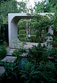 Langer schmaler Garten mit massiven Einrahmungen aus Beton, Farne, Wasser und Papyrus