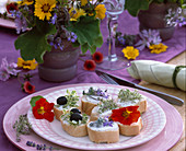 Teller mit Baquettehäppchen, Zitronenthymian, Basilikum 'Pesto Perpetuo', Blüten von Borretsch und Kapuzinerkresse und schwarze Oliven