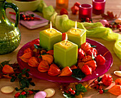 Glasteller mit grünen Kerzen, Physalis (Lampions), Hedera (Efeu), Rosa (Hagebut)