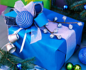 Blaues Geschenk mit Eucalyptus, Baumkugel, silbernen Töpfchen, Schleifenbändern