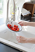 Hands washing colander of strawberries in running water