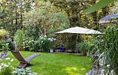 Wooden lounger on lawn and parasol in well-tended garden