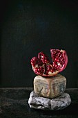 Aufgeschnittener Granatapfel auf dekorativen Steinen vor schwarzem Hintergrund