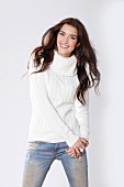 A brunette woman wearing a white cable-knit jumper and jeans