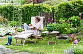 Idyllischer Schrebergarten im Frühling mit Frau auf Holzliegestuhl