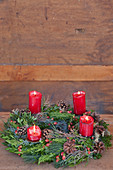 Adventskranz mit brennenden roten Kerzen vor einer Holzwand