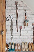 Various accessories and jewellery hung from vintage hooks on brick wall above collection of high-heeled shoes