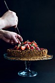 A chocolate cake topped with strawberries, pomegranate seeds and nuts