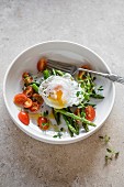 A poached egg on a bed of asparagus with cherry tomatoes
