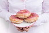 Frau hält einen Teller mit rosa glasierten Doughnuts