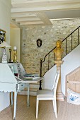 Antique bureau at foot of staircase with stone wall in traditional country house
