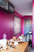 Blick von Esstisch auf pinkfarbene Wänden mit gerahmtem Brokatmuster und Eingangstür