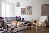 Arc lamp and rocking chair with sheepskin blanket in cosy, candlelit living room