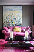 Pinkfarbene Couch mit Kissen und schwarzer Couchtisch vor Gemälde mit moderner Malerei