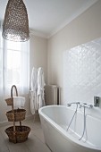 Free-standing white bathtub, dressing gowns and baskets in bathroom