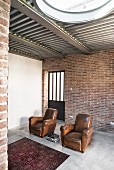 Two vintage leather armchairs on concrete floor against brick wall