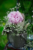 Tin can filled with peonies and flowering chervil on garden chair