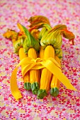 A bunch of yellow courgettes with flowers tied together with a ribbon on a floral tablecloth
