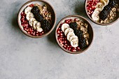 Three oatmeal bowls topped off with blackberry, banana, and pomegranate seeds