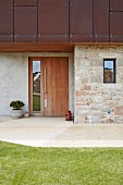 Holztür in moderner Fassade aus rostigem Metall, Naturstein und Beton