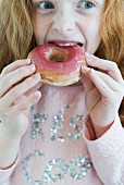Kleinen Mädchen isst rosa glasierten Doughnut