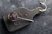 Poppy seeds on a spoon on a wooden board with a black background